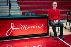 IU Southeast Coach Jim Morris sits on the sidelines of a basketball court.